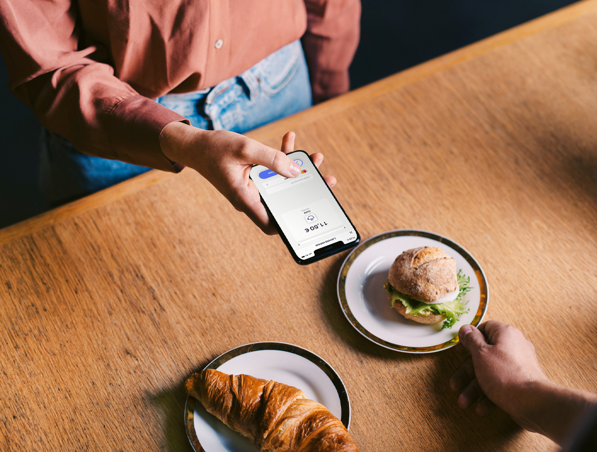 Nainen maksaa välipalan MobilePay sovelluksella kahvilassa