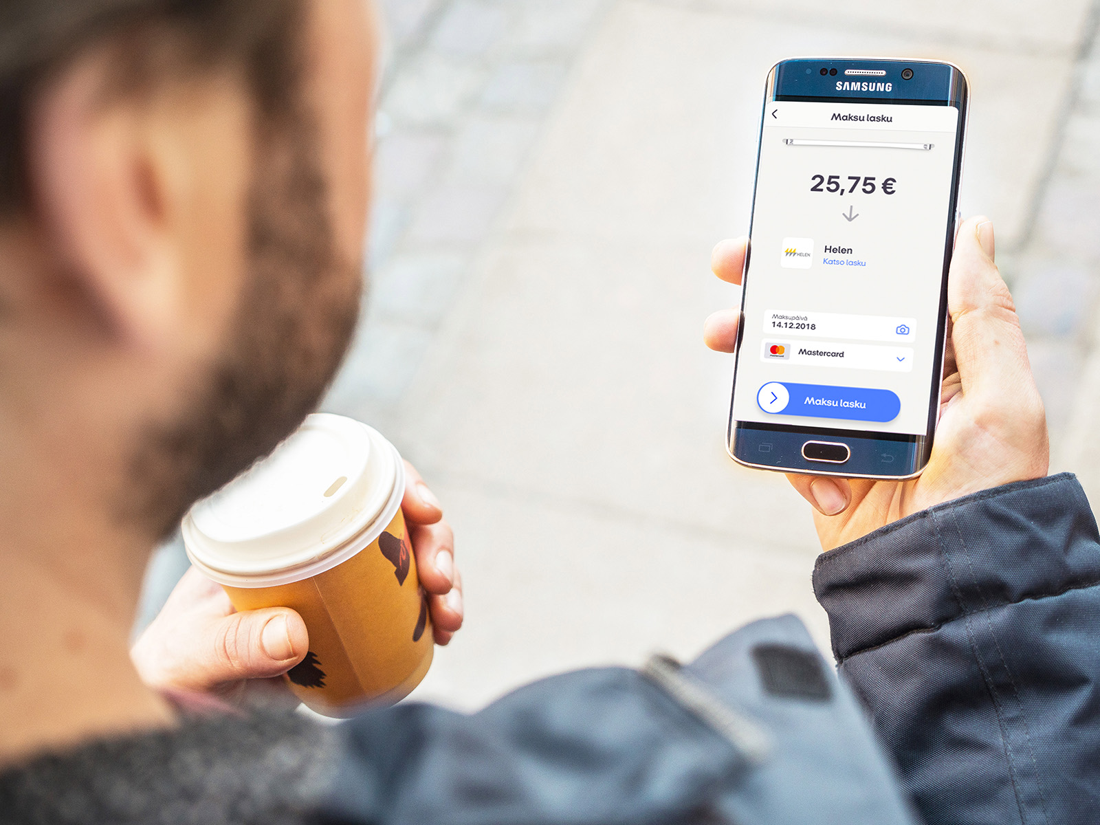 Mies kahvikuppi kädessä maksamassa laskua MobilePay sovelluksella