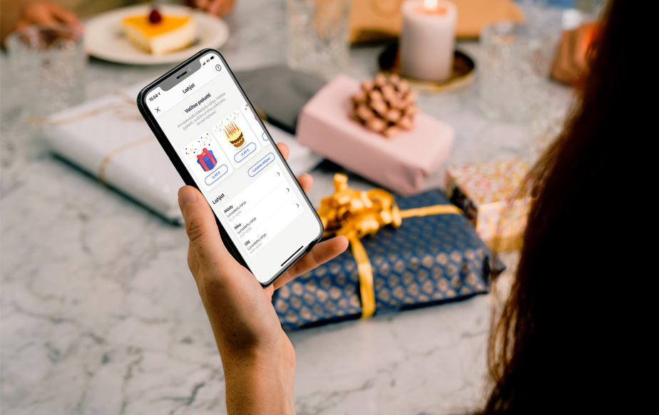 Henkilöllä puhelin kädessä lahjapöydän ääressä, MobilePay sovellus auki rahaa lahjaksi näkymässä