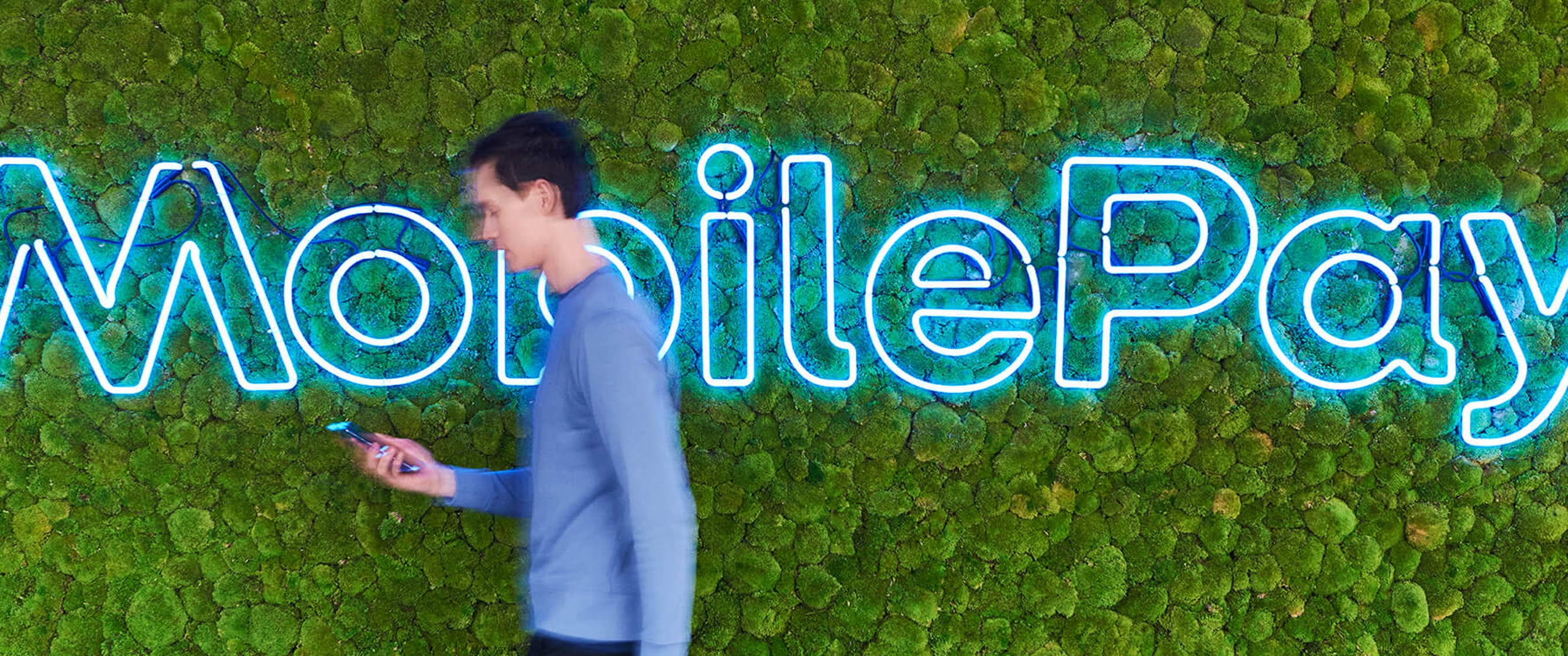 Boy walking in front of blue MobilePay Sign with his phone.