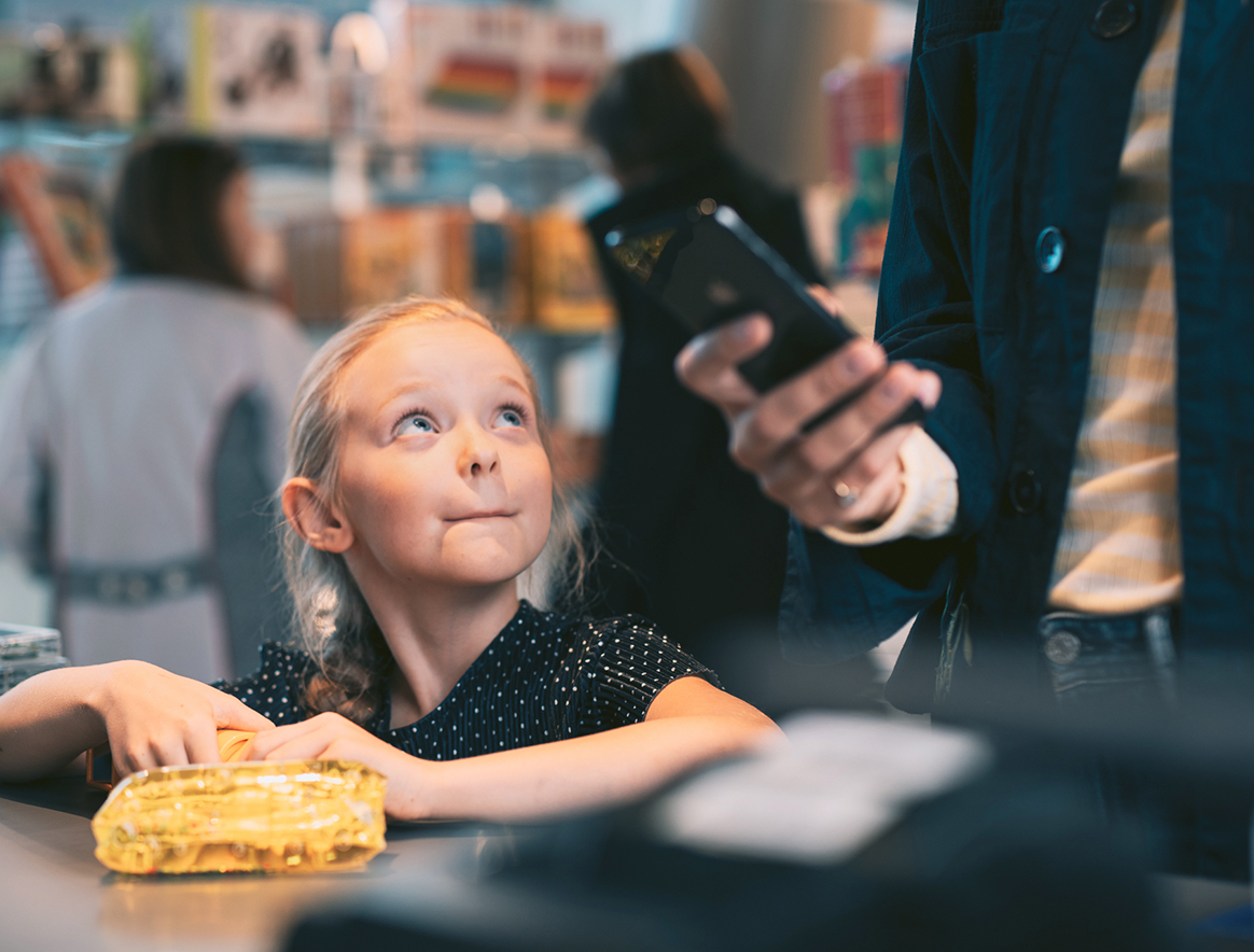 Nainen ja lapsi lelukaupassa. Nainen maksaa ostoksia MobilePaylla.